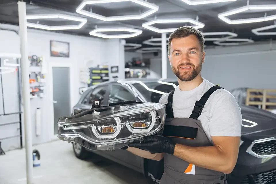 smiling-auto-mechanic-holding-car-headlight Muffler Shops Near Me: Why is Your Muffler Important?