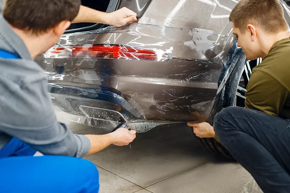 two-workers-applies-car-protection-film-on-bumper مزایای صافکاری درب ماشین بدون رنگ